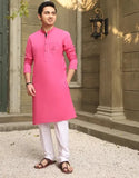 Man wearing a pink kurta with white pants standing outdoors.
