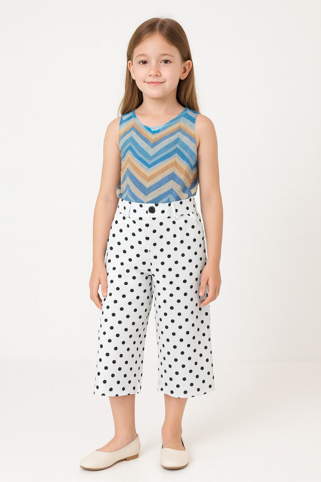 Young girl wearing a sleeveless top with a zigzag pattern and polka dot pants on a white background