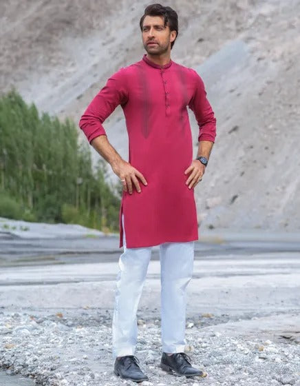 Man wearing a red kurta with white pants standing outdoors.
