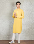 Man wearing a yellow kurta with white pants against a textured gray wall.