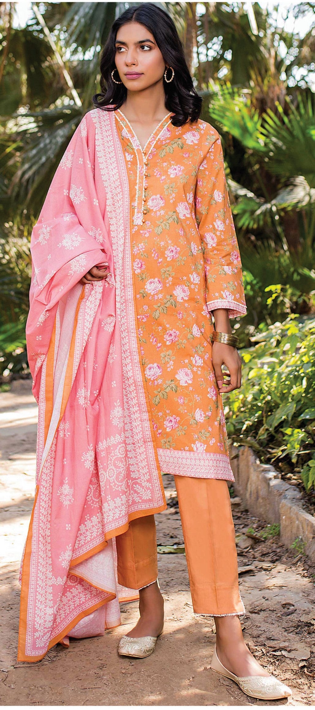 Woman wearing a pink and orange traditional outfit with a floral pattern in a natural setting.