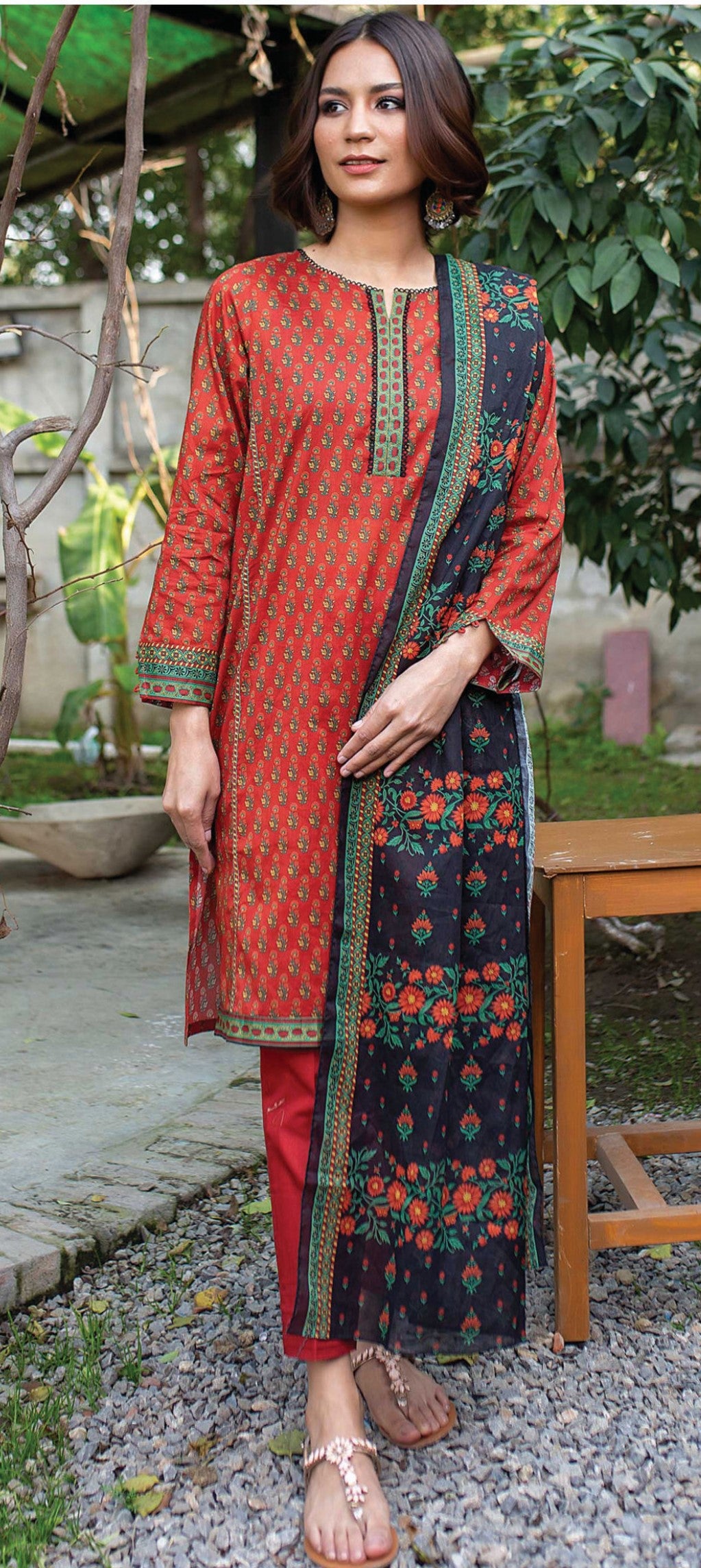 Woman wearing a traditional outfit with red and black patterns in an outdoor setting.